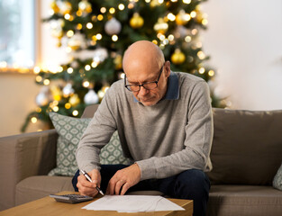 Sticker - winter holidays, finances and people concept - senior man with papers or bills and calculator writing at home in evening over christmas tree lights on background