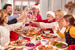 © Monkey Business - Multi Generation Family In Santa Hats Making Toast Whilst Eating Christmas Meal At Home Together