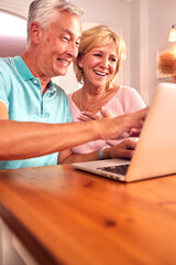 Wall Mural - Senior Retired Couple Sitting On Sofa At Home Shopping Or Booking Holiday On Laptop