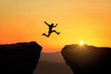 Fototapeta  - Man jumps from cliff to cliff over a precipice at sunset, a creative idea. Success and Risk Concept