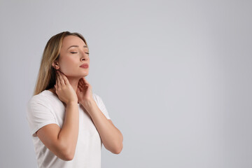 Wall Mural - Young woman doing thyroid self examination on light grey background, space for text