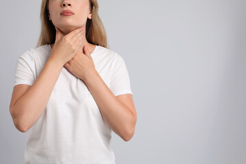 Young woman doing thyroid self examination on light grey background, closeup. Space for text