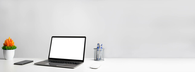 Working concept using technology, notebook, smartphones, devices. Blank white screen laptop on a white table in the office. Copy space on right for design or text, Closeup, Gray, and blur background