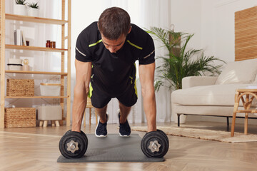 Canvas Print - Handsome man doing plank exercise with dumbbells on floor at home