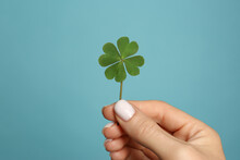 Woman Holding Green Four Leaf Clover On Light Blue Background, Closeup