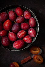 Freshly Picked Red Plums In A Vintage Baking Tin. Several Plums Are Cut Open At The Side.