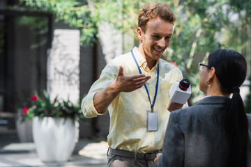 Poster - happy reporter gesturing while taking interview with blurred asian businesswoman in glasses