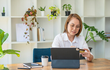 Serious focused middle aged female accountant in eyewear working from home providing outsource bookkeeping service, sitting at table with portable computer, calculating finances, doing paperwork