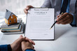 © crizzystudio - Real estate agent home sales broker is using a pen pointing to the contract document house model and explains the business contract, rent, buy, mortgage, loan, or home insurance