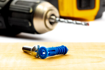 macro close up view of a plastic concrete wall anchor and screw with an electric drill and concrete drill bit out of focus in the 

background
