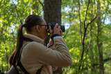 Fototapeta Na ścianę - Woman photographer walking and taking picture photo of forest landscape on camera. Shooting nature.