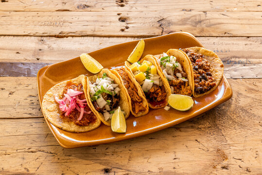 Clay tray with assorted Mexican tacos of cochinita pibil, pastor tacos, lime, chicken tinga, chili con carne and beans