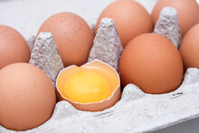 A Brown Chicken Egg Is Half Broken Among Other Eggs In A Carton Tray
