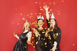© vladdeep - Three delighted women in black dress and party hats over red background with golden confetti. Female party