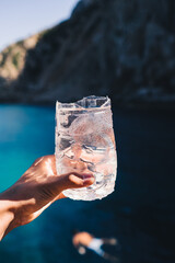 Sticker - Vertical shot of a man keeps a fresh cocktail on the ocean background