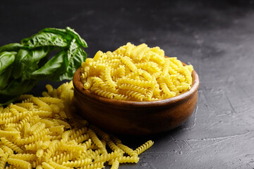 Girandole pasta in wooden bowl and green basil herb on black table