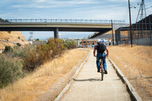Photo Of A Young Man In A Baseball Cap And Backpack Biking Along The American River Parkway Trail In Sacramento, California, U.S.A.