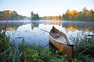 Wall Mural - yellow canoe on shore of calm lake with island at sunrise during autumn