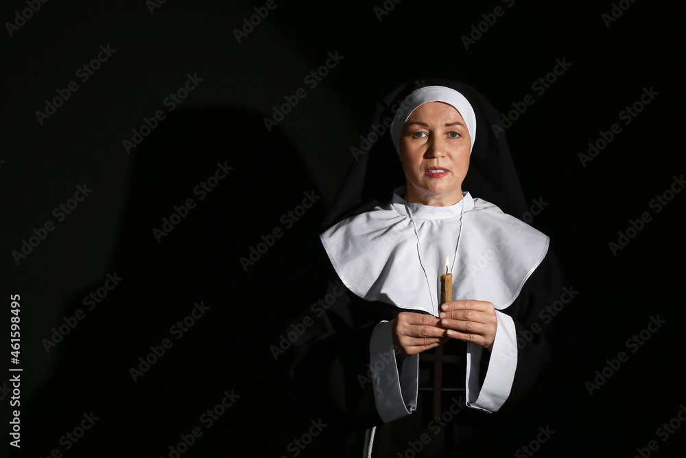 Mature nun with burning candle on dark background