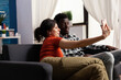 © DC Studio - Cheerful interracial couple taking pictures with smartphone at home. Multi ethnic people making memories and selfies with modern device in hand and technology. Mixed race happy partners