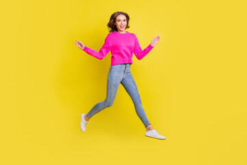 Wall Mural - Full length photo of sweet adorable wavy young woman wear pink sweater jumping walking isolated yellow color background