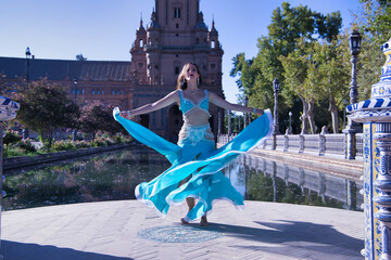 Wall Mural - Middle-aged Hispanic woman in turquoise dress with rhinestones, twirling holding her dress while belly dancing. Belly dance concept.