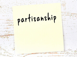 Yellow sticky note on wooden wall with handwritten word partisanship