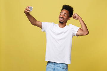 young afro american black man smiling happy taking selfie self portrait picture with mobile phone looking excited having fun posing cool isolated in yellow background in communication technology