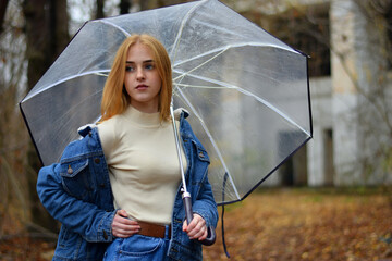 young girl with umbrella walking in at beautifu autumn park. modern girl in casual clothes walks through the city park. Seasonal style, autumn beauty. autumn season, in a blue jacket, in autumn leaves