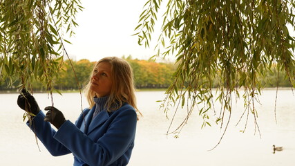 Woman in the park standing with a pensive view against the backdrop of a pond and autumn trees with orange foliage.Outdoor recreation concept