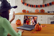 © Studio Romantic - Group of people happy to see each other at virtual Halloween party. Young girl sitting in front of laptop computer at decorated kitchen table, waving hand and greeting friends at online video meeting