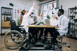 © sofiko14 - Diverse group of qualified doctors smiling cheerful and gesturing with arms raised while sitting at conference room. Progress and success in medical research. International cooperation.