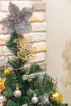 Christmas tree-topper in shape of a star or bow decorating xmas fir tree with the gold and silver baubles, multi-colored bows, animals, bells, lit garlands against the decorative brick wall background