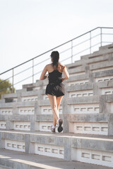 Sticker - Vertical shot of a healthy adult Asian female running up on concrete stairs of the city stadium