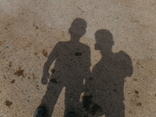 Shadows Of Two Boys Standing Above Grey Dirt Ground