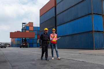 Industrial worker works with co-worker at overseas shipping container yard . Logistics supply chain management and international goods export concept .