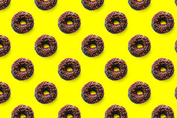 Wall Mural - Black donuts with red glaze on yellow background seamless pattern top view. Food dessert flatly flat lay of delicious sweet nibbles chocolate donuts