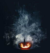 Spooky Halloween Jack O Lantern Pumpkin With Carved Scary Grinning Face Glowing In Smoke On Halloween Night.