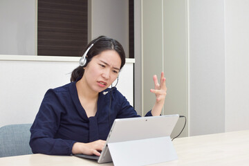 A young Asian woman wearing a headset gets angry at her customer during telework at home