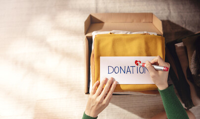 Wall Mural - Clothes Donation Concept. Box of Cloth with Donate label. Woman Preparing Used Old Garment at Home. Top View