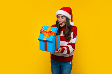 Wall Mural - Close up photo of beautiful excited smiling woman with Christmas gift box in hands is having fun while posing on yellow background