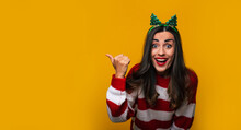 Happy Attractive Funny Young Woman In Christmas Tree Hat On Her Head While She Is Pointing Away Isolated On A Yellow Background And Having Fun