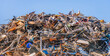Large heap of old iron objects intended for recycling against a bright blue sky. The photo was taken in the Netherlands on a sunny day in autumn.