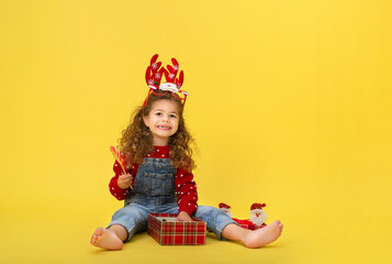 Wall Mural - Portrait of happy little  girl Christmas  holding present box and looking at camera on yellow background
