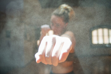 Front view of young sportswoman applying glove starch. Attractive woman in sport clothes in gym punching at camera. Sport, healthy lifestyle, boxing concept