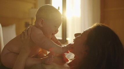 asian woman mother holding baby infant in arm playing and talking with kid on sofa couch in living r