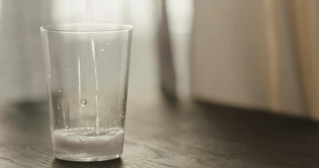 Wall Mural - Slow motion pour sparkling water in tumbler glass on black oak table with copy space