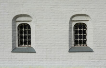 Fragment Of The White Wall Of An Old Brick Building. Traditional Russian Architecture. There Are Two Windows With Bars. Background. Texture