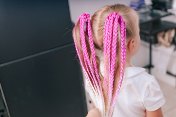 Colored  braids in a pink shade in a hairstyle on a blonde girl