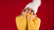 © Alexander - young sweet and smiling blonde woman in a yellow knitted sweater on a red background, wrapped in a collar. A blonde in a yellow jacket and a white hat on a red background
